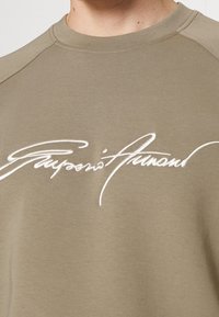 Olivgrön sweatshirt med rundad halsringning. Funktioner vit broderad text på framsidan. Tillverkad av mjukt tyg med en slät struktur.