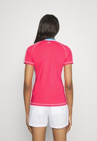 Zadní pohled na růžové atletické tričko s krátkými rukávy, s modrým límcem a bílými akcenty, vyrobené z hladké, lehké tkaniny.