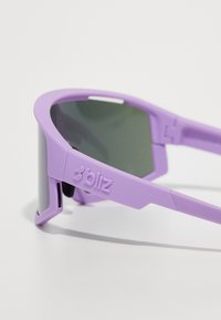 Lila Sonnenbrille mit einem eleganten Design, ausgestattet mit einer matten Oberfläche und grauen Gläsern. Enthält ein markantes Logo an der Seite des Rahmens.