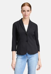 Zwarte blazer met een sjalkraag en twee knopen, gemaakt van een textuurstof en met driekwartmouwen, gecombineerd met lichtblauwe jeans.