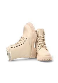 Botas de tobillo beige fabricadas con material sintético suave, con suela gruesa, diseño de cordones y puntera redondeada con costuras detalladas.