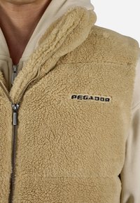 Beige vilnas veste ar augstu apkakli, ar priekšējo rāvējslēdzēju un zīmola nosaukumu "PEGADOR" izšūtu melnā krāsā. Mīksta, teksturēta virsma.