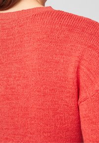 Pull en tricot rouge avec une finition texturée, doté d'un col rond et de détails de couture visibles le long des coutures.