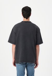 Dark gray oversized t-shirt with short sleeves and a crew neckline, featuring visible stitching details and a relaxed fit.