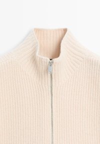 Light pink zip-up sweater with a high collar, featuring a ribbed texture and a silver zipper. Simple, clean design.