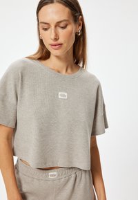 Lichtgrijze geribde gebreide cropped t-shirt met een ronde hals, los vallende mouwen en een klein labeldetail aan de voorkant.