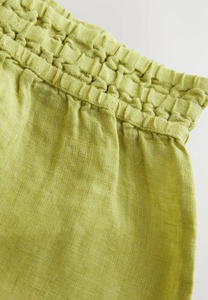 Ljust grönt linnetyg med detaljer i smock i midjan. Texturen är något rynkig, vilket visar på en naturlig, andningsbar kvalitet.