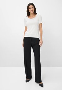 Witte top met korte mouwen en een ronde hals, gedragen met zwarte, rechte broek. De outfit heeft een gladde textuur en minimale details.