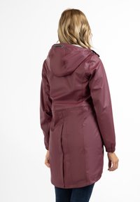 Jachetă de ploaie marron cu glugă, manșoane elastice și talie ajustată, înfățișând un material neted, waterproof și detalii cu pliuri în spate.