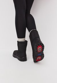 Botas de invierno aisladas en negro con un upper texturizado, cierre de cremallera y acentos en rojo y azul en la suela de goma.
