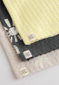 Pile de trois tissus texturés : beige, gris foncé avec un motif de soleil blanc, et jaune pâle, chacun avec une petite étiquette affichant des lignes ondulées.