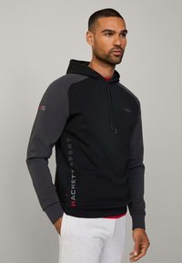 Sudadera con capucha en negro y gris, con una tela texturizada, que cuenta con detalles en rojo y un logotipo impreso en el lado y el pecho.
