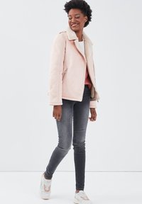 Chaqueta de ante sintético rosa con cuello de borreguillo, bolsillos con cremallera en el frente, combinada con jeans ajustados grises y zapatillas blancas.