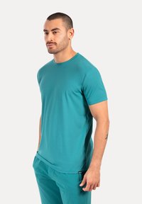 Camiseta de manga corta color turquesa, confeccionada en tejido suave y ligero; cuenta con un cuello redondo y un corte relajado, combinada con pantalones a juego.
