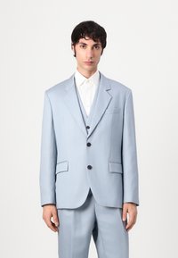 Traje de tres piezas azul claro hecho de tela suave, con un blazer de un solo botón que tiene dos bolsillos frontales y botones negros.