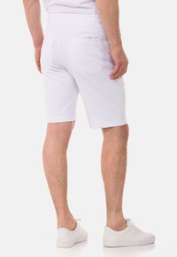 Weiße Shorts mit einem figurnahen Schnitt, hergestellt aus weichem Material. Verfügt über einen Kordelzug in der Taille und zwei Gesäßtaschen. Getragen mit weißen Sneakern.