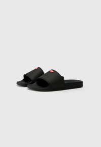 Black rubber slides with an open toe design, featuring a wide upper strap. A small red logo is visible on the front of the left sandal.