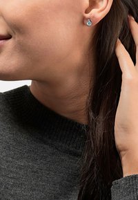 Silberne Ohrstecker mit Aquamarinsteinen, runde Form und strukturiertes Design, getragen von einer Person mit dunklen Haaren, die einen dunklen Pullover trägt.