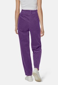 Pantaloni in corduroy viola con vita alta e vestibilità rilassata, caratterizzati da righe verticali. Abbinati a sneakers bianche.
