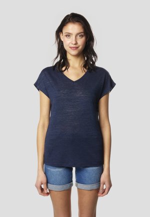 Temno modra T-majica z V-izrezom in kratkimi rokavi, izdelana iz mehke, lahke tkanine, kombinirana z jeans kratkimi hlačami s podvitimi robovi.