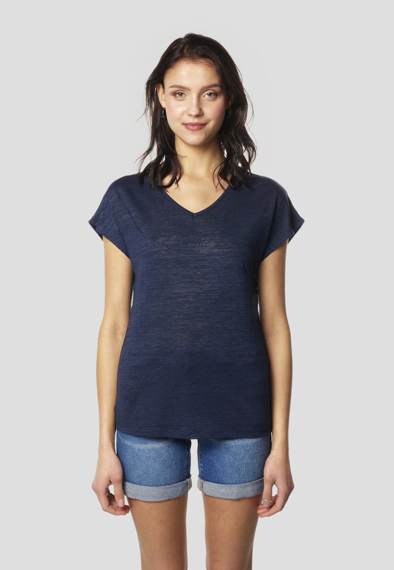 Tmavomodré tričko s výstrihom do V a krátkymi rukávmi, vyrobené z mäkkej, ľahkej látky, skombinované s džínsovými šortkami s obrúbenými nohavicami.