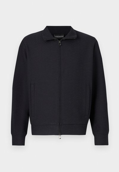 Giacca nera con cerniera, motivo testurizzato, collo alto, tasche laterali e polsini a coste. Realizzata in morbido tessuto intrecciato.