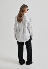White long-sleeve shirt with vertical black stripes, relaxed fit, paired with black wide-leg pants. Simple design and tailored cuffs.