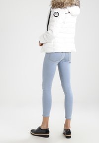 Bílá péřová bunda s umělou kožešinou na kapuci, černými zipy, spárovaná se světle modrými skinny džíny a černými botami s béžovou podrážkou.