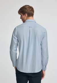 Ljust blå långärmad skjorta med knappar, bakparti med yoke-detalj och enknappssmanchetter. Slät tyg med en lätt avslappnad passform.