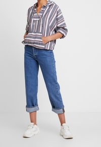 Grau gestreifter Kapuzenpullover mit rosa und weißen Streifen, kombiniert mit hellblauen Jeans mit hochgekrempelten Ärmeln und weißen Sneakers.