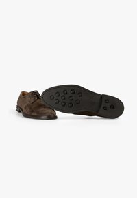 Zapatos de ante marrón con puntera redondeada, que presentan un diseño de cordones y pequeños acentos circulares de caucho sobre una suela negra.