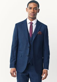 Costume ajusté bleu marine en tissu texturé, comprenant un blazer à boutonnage simple, trois boutons et un gilet assorti ; cravate bordeaux.