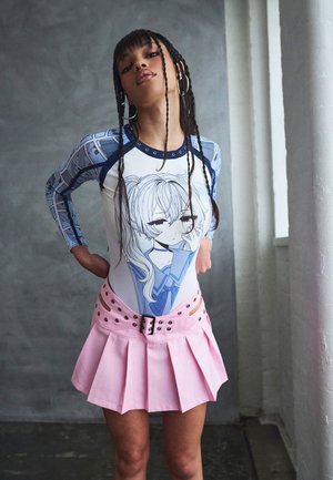 Ung person med lange fletninger iført en blå og hvid t-shirt med anime-grafik og en pink plisseret mininederdel med bælte detaljer.