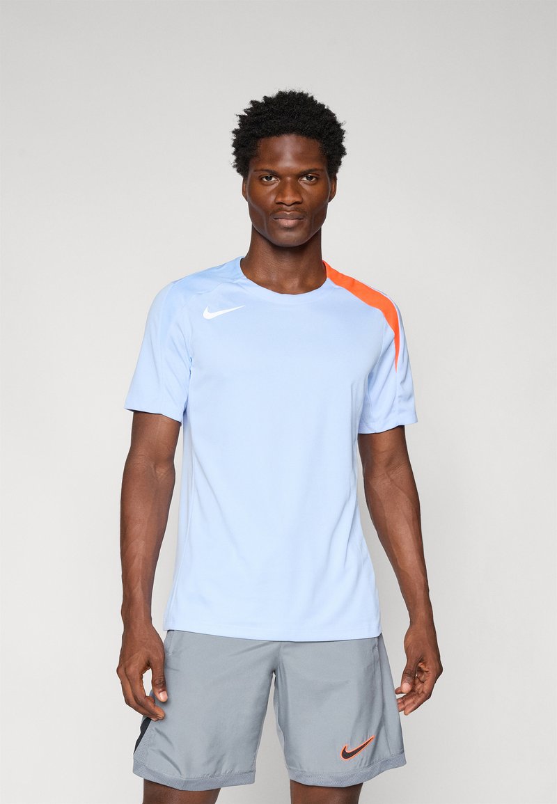 Light blue athletic t-shirt with a red-orange accent on one shoulder, featuring a small white Nike logo on the chest.