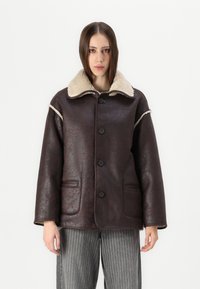 Bruine shearling gevoerde jas met een grote kraag, vijf knopen, twee voorzakken en een licht oversized pasvorm. Geweven finish overal.
