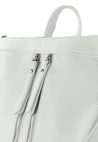 Witte gestructureerde leren tas met een hoek, voorzien van zilveren ritsen en ritsen, een handvat en nauwkeurige stiksels voor extra detail.