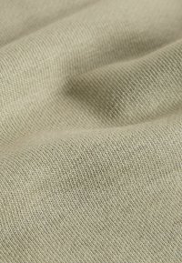 Tissu tricoté beige avec une texture fine et uniforme, des plis doux créant des ombres et des reflets délicats.