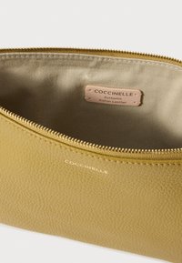 Geel, getextureerd leren etui met een gouden rits, voorzien van een binnenlabel met de tekst "Coccinelle, Authentiek Italiaans Leer."