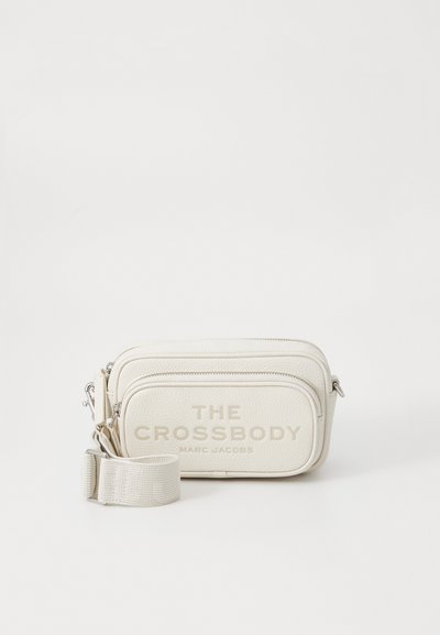 Crossbody tas in gestructureerd crème leer met twee ritssluitingen, verstelbare schouderband en geperste letters aan de voorkant.