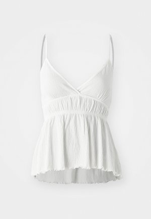 Top sans manches blanc avec un décolleté en V, en tissu texturé et taille froncée. Présente un ourlet évasé et de fines bretelles ajustables.