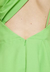 Grön klänning med djup v-ringning, dold dragkedja och rynkade tygdetaljer. Tillverkad av ett mjukt och lätt material.