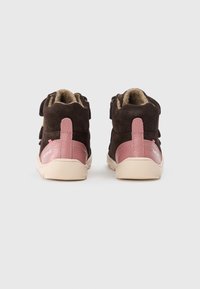 Botas de tobillo de ante marrón con detalles de cuero rosa, suelas de goma beige y forro interior de felpa. Cuenta con una pestaña en la parte posterior para ponerlas con facilidad.