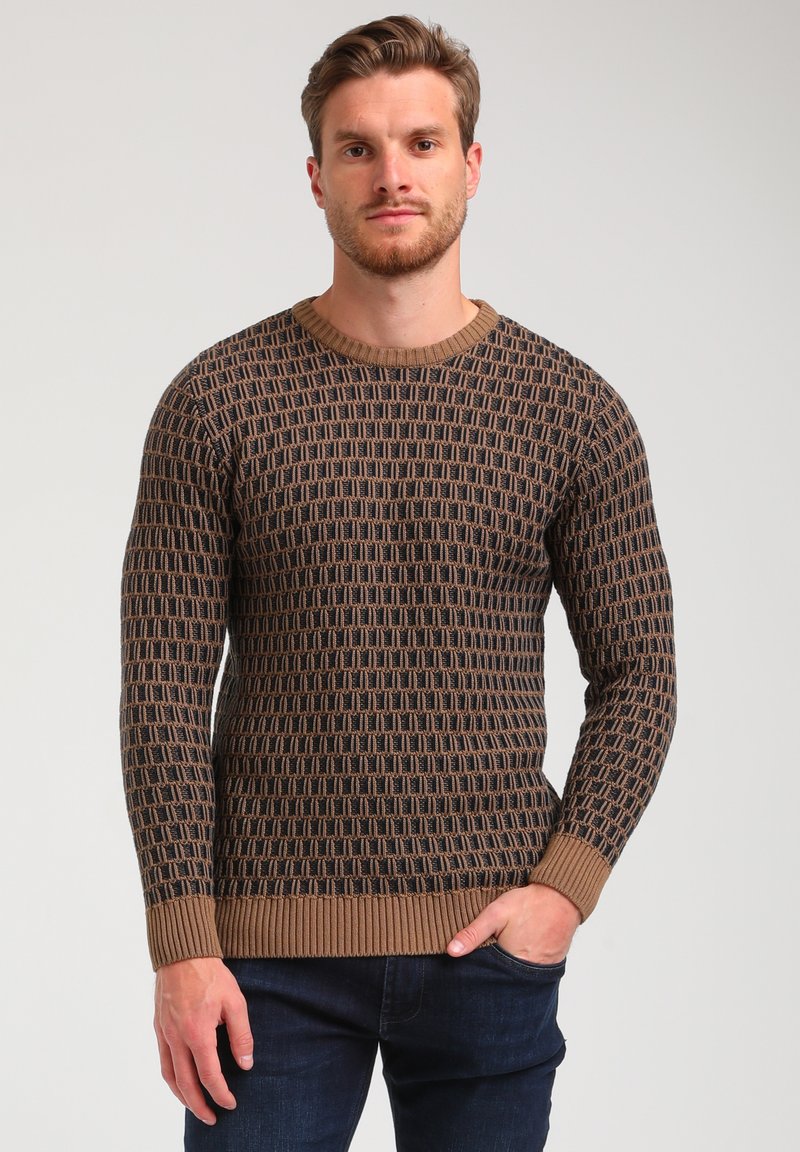 Brauner Strickpullover mit strukturiertem geometrischem Muster, runder gerippter Ausschnitt und gerippten Bündchen, kombiniert mit dunklen Jeans.