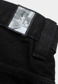 Tela de mezclilla negra con una etiqueta texturizada en la cintura y un estampado gráfico en gris. El diseño presenta detalles de costura y un acabado limpio.