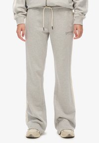 Gray sweatpants made of soft fabric, featuring a drawstring waist, side stripes, and a small logo on the front. Flared leg design.