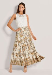 Weißes ärmelloses Oberteil mit Spitzenverzierungen am Ausschnitt, kombiniert mit einem langen, gemusterten Rock mit Paisleymustern in erdigen Farben.