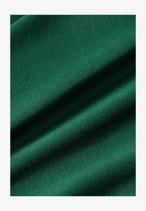 Zaļa auduma virsma ar gludu, viegli teksturētu struktūru, kurā redzamas maigas krokas un vieglas ēnas.