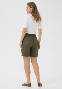 Shorts vert olive avec une taille élastique, assortis d'un haut blanc ajusté. Le design est décontracté avec une coupe droite et une silhouette à hauteur de genou.