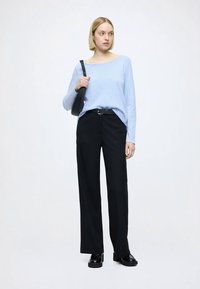 Lys blå genser med lange ermer og firkantet hals, kombinert med svarte bukser med vide ben. Modellen holder en svart skulderveske; blanke sko fullfører antrekket.