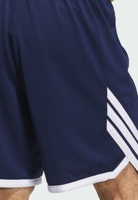 Pantalones cortos deportivos azul marino hechos de material de malla, con acentos de franjas blancas a los lados y un ribete blanco en el dobladillo.